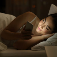 Entspanntes Mädchen mit einem Smartphone, das nachts auf dem Bett liegt