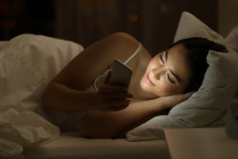 Entspanntes Mädchen mit einem Smartphone, das nachts auf dem Bett liegt