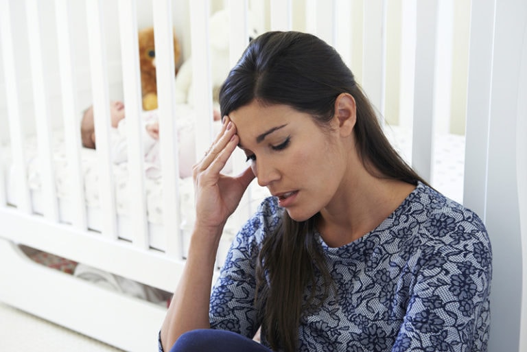 frustrierte Mutter sitzt neben der Krippe