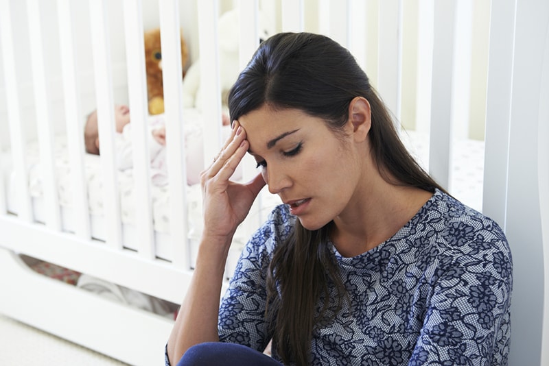 frustrierte Mutter sitzt neben der Krippe