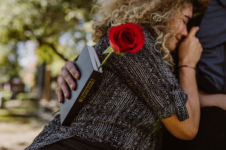 eine Person, die eine Bibel hält und eine weinende Frau umarmt