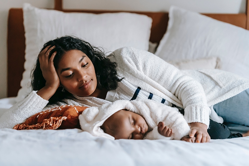 Mutter schaut ihr schlafendes Baby an, das auf dem Bett liegt
