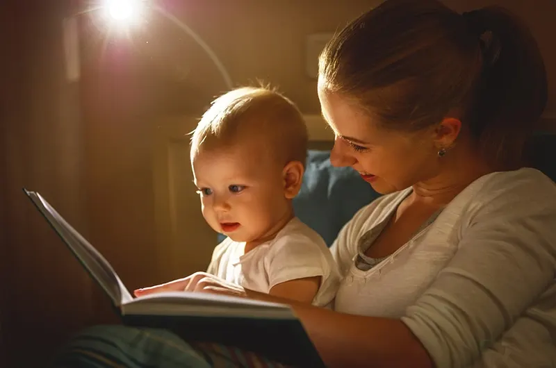 Mutter und Babysohn lesen ein Buch im Bett, bevor sie schlafen gehen