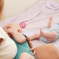 Mutter, die ihr Kind stillt, während das andere Baby auf dem Bett weint