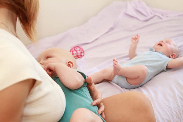 Mutter, die ihr Kind stillt, während das andere Baby auf dem Bett weint