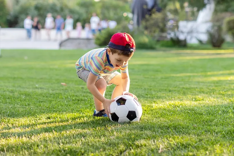 kleiner Junge, der Fußball im Park spielt