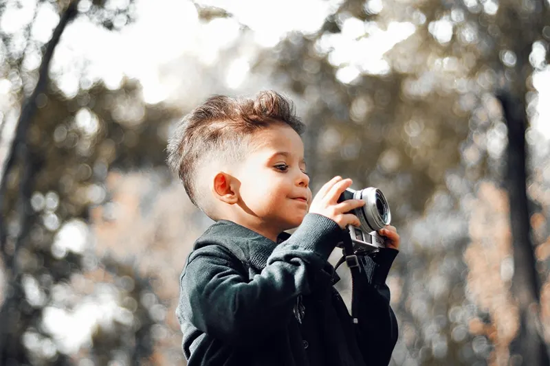 kleiner Junge hält eine Kamera im Freien