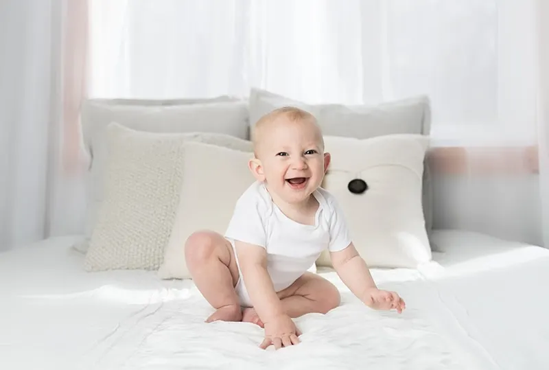 Baby Junge sitzt auf dem Bett und lächelt
