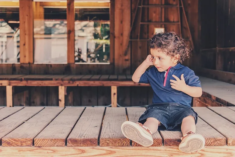 kleiner Junge sitzt auf der Holztheke und schaut beiseite
