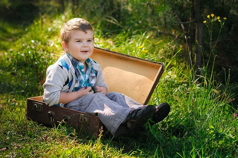 kleiner Junge sitzt im Koffer auf dem Gras