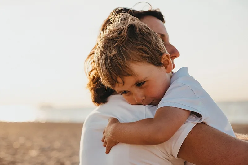 kleiner Junge umarmt seine Mutter am Strand