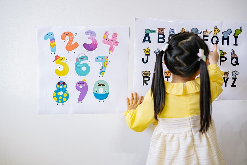 kleines Mädchen im gelben Kleid liest Alphabet an der Wand