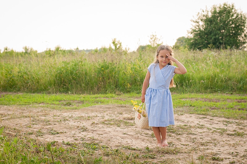kleines Mädchen mit Handtasche auf dem Feld stehen