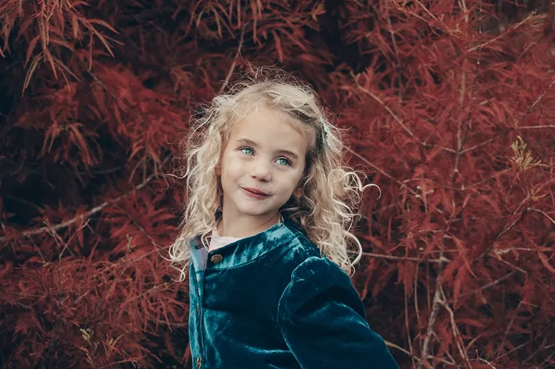 kleines Mädchen mit blauen Augen, das in der Nähe des Baumes steht