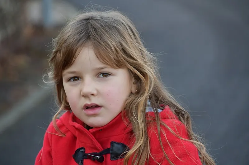 kleines Mädchen mit rotem Mantel, das auf der Straße steht