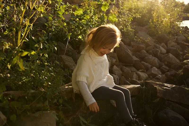 kleines Mädchen mit weißem Pullover sitzt auf dem Felsen