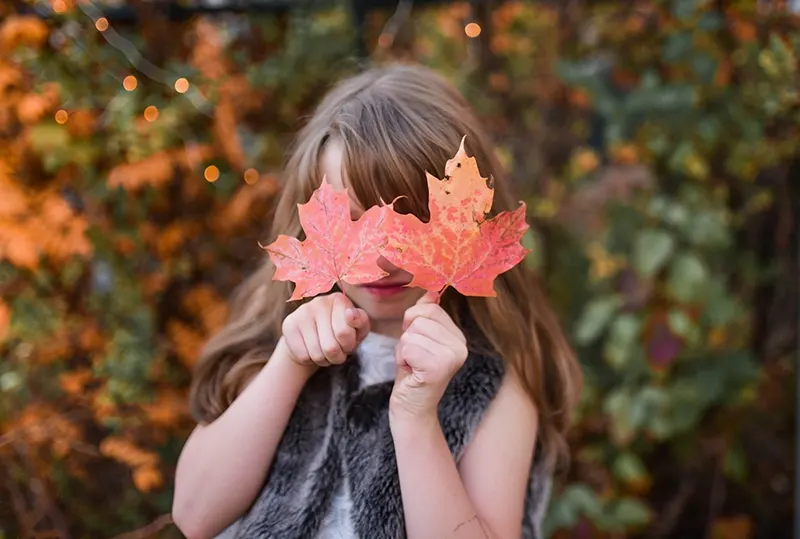 kleines Mädchen verstecktes Gesicht mit getrockneten Blättern