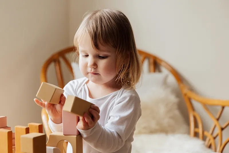 konzentriertes kleines Mädchen, das zu Hause mit Holzmädchen spielt