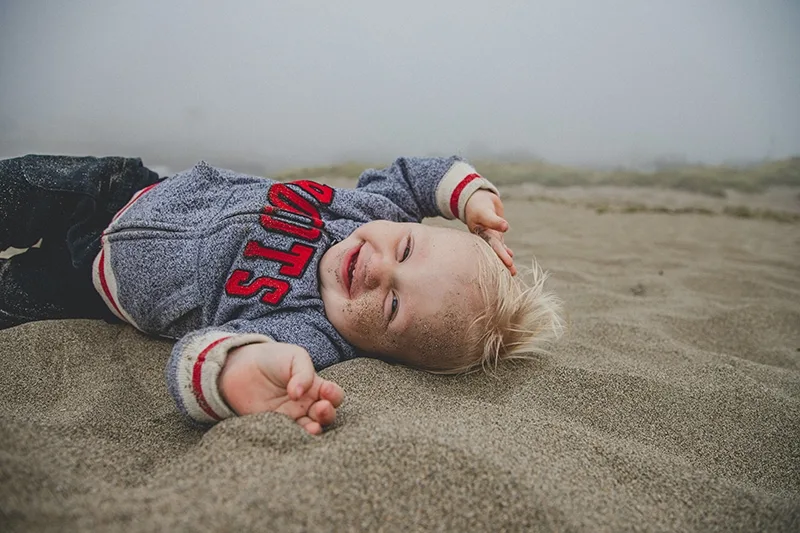 lächelnder blonder kleiner Junge, der auf dem Sand liegt