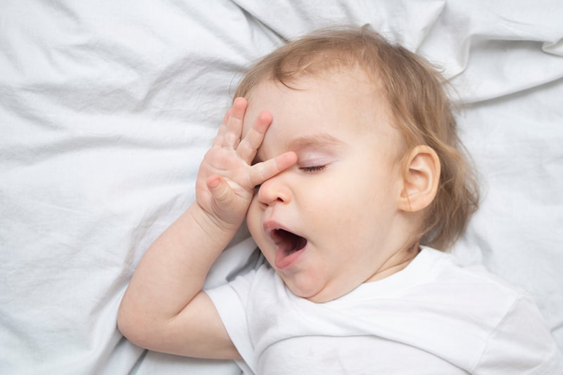schläfriges Baby reibt sich die Augen und gähnt
