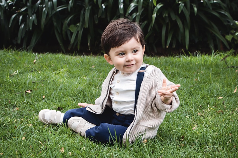 süßer kleiner Junge in einem Pullover, der auf dem Gras sitzt