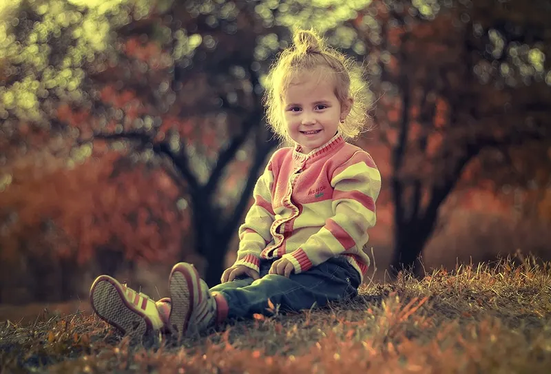 süßes Mädchen im Pullover sitzt auf dem Gras