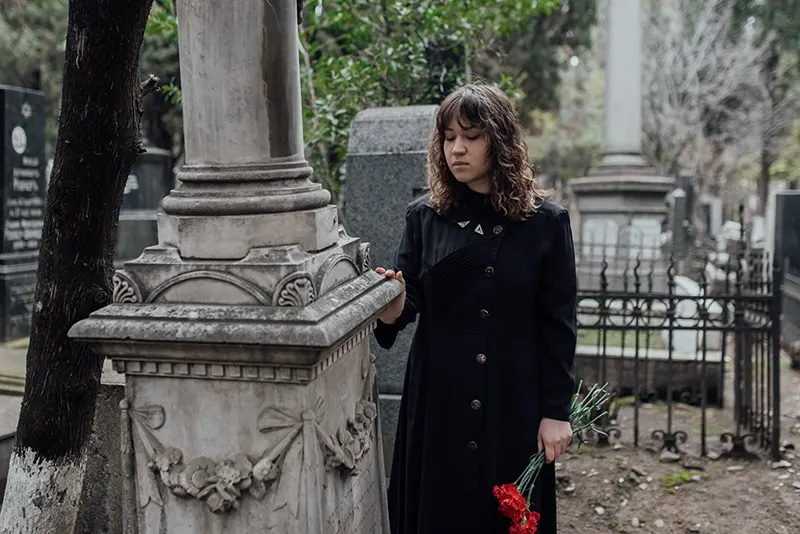 traurige Frau, die auf dem Friedhof steht und Blumen hält