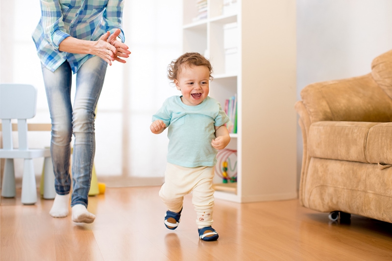 Baby Kleinkind hat Spaß beim Laufen im Wohnzimmer mit seiner Mutter