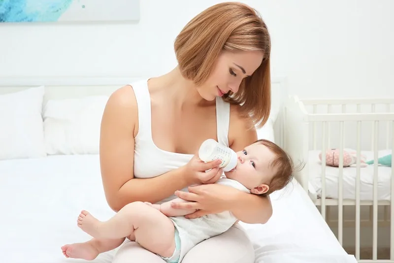 Frau, die Baby mit Säuglingsmilch füttert, während sie auf dem Bett sitzt