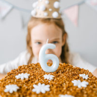 ein Mädchen hinter Geburtstagstorte zu ihrem 6. Geburtstag