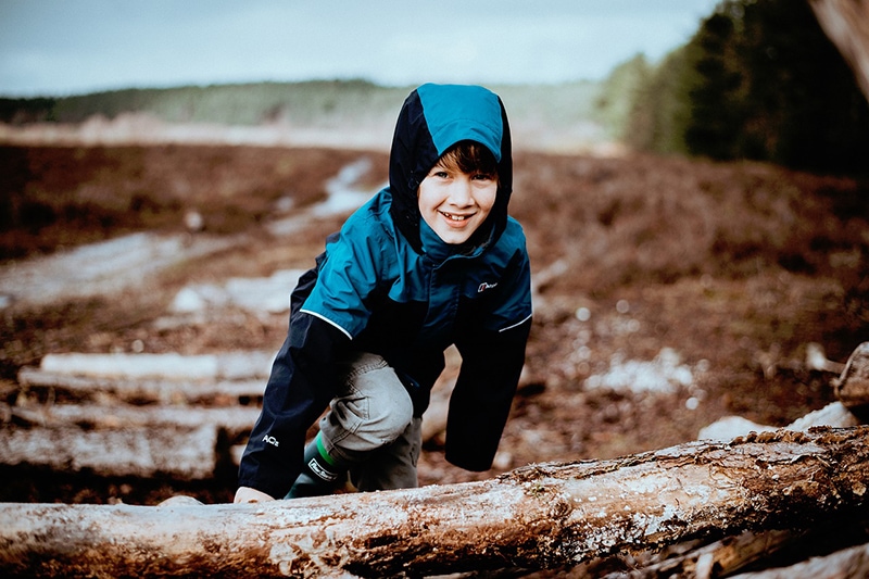 Junge in blauer Jacke klettert auf Holzstamm