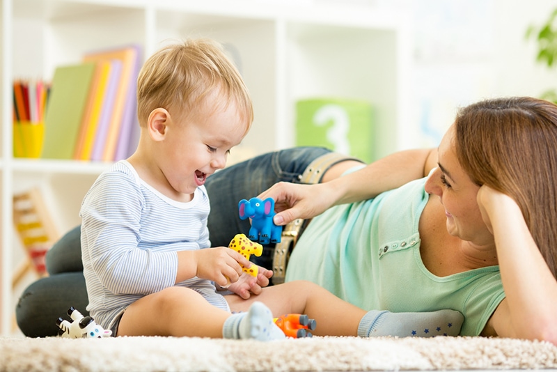 Kind und Mama spielen mit Spielzeugtieren auf dem Teppich zu Hause