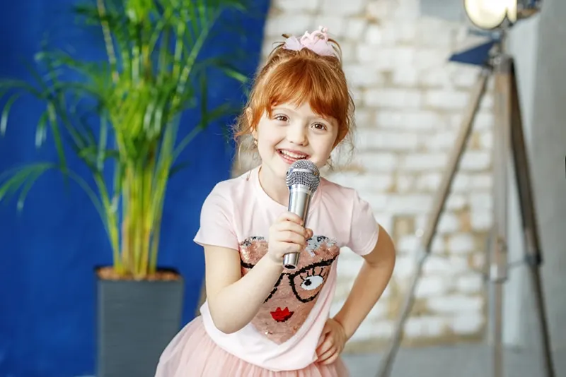 Lächelndes kleines Mädchen, das ein Lied in ein Mikrofon singt