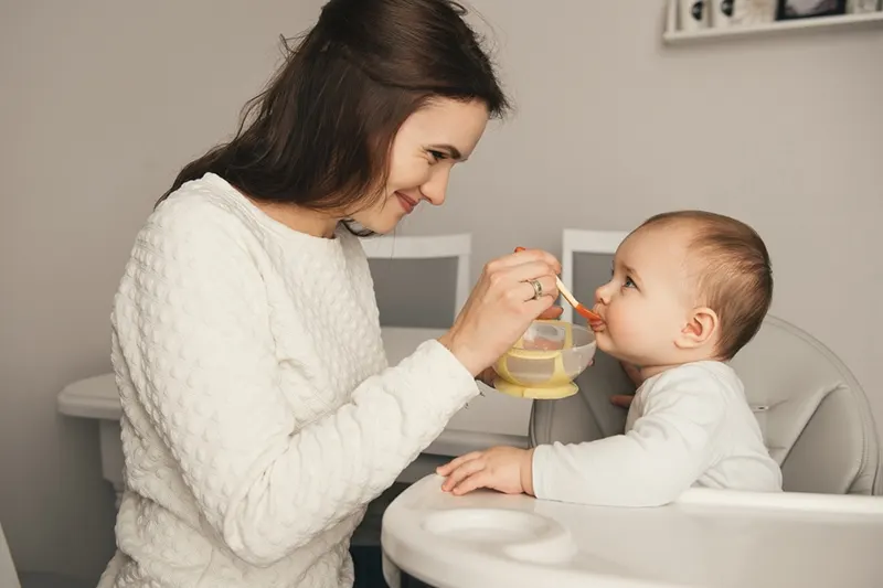 Mutter füttert ihr Baby im Futterstuhl sitzend