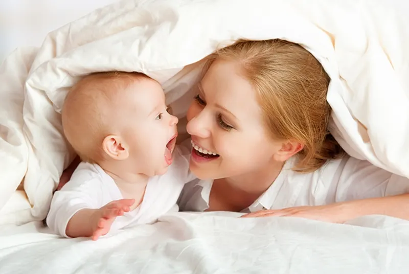 Mutter und Baby spielen und lächeln unter einer Decke