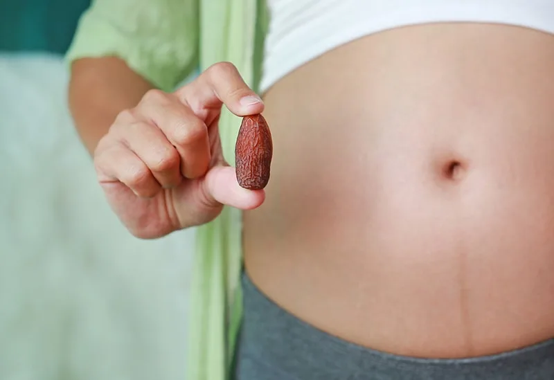 Schwangere Frau mit süßen getrockneten Dattelpalmenfrüchten vor ihrem Bauch