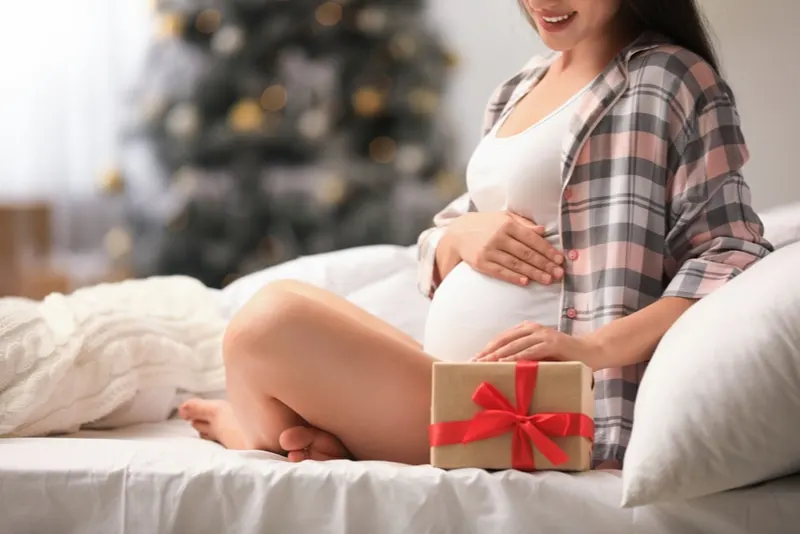 Schwangere posiert neben einem Weihnachtsgeschenk
