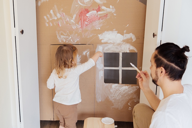 Vater malt Papphaus mit kleiner Tochter
