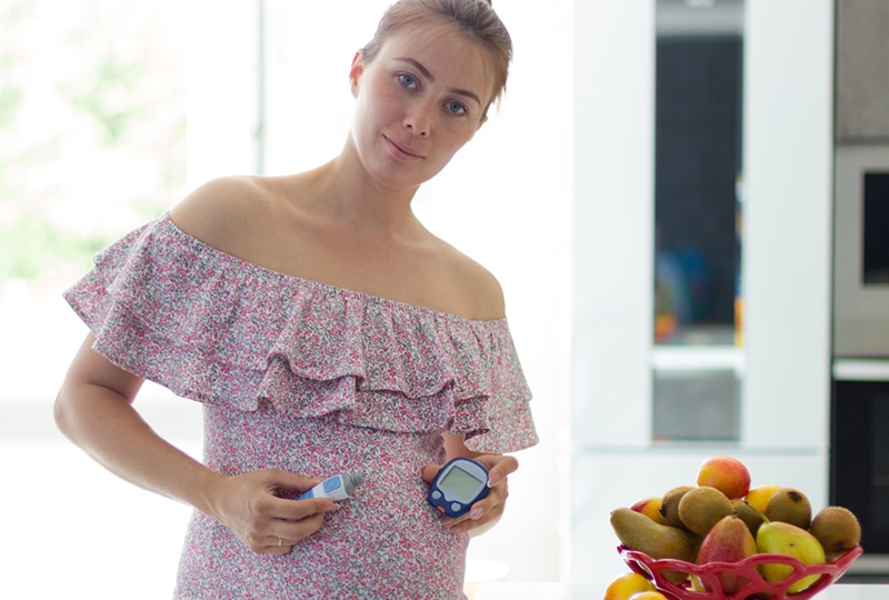 eine schwangere Frau mit einem Blutzuckermessgerät, die neben einer Schüssel mit Früchten steht