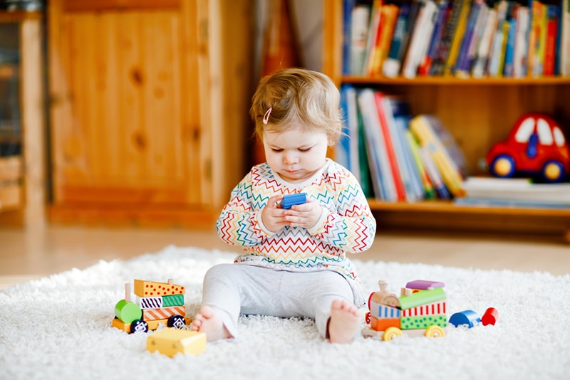 kleines Mädchen, das zu Hause mit pädagogischem Holzspielzeug auf dem Teppich spielt