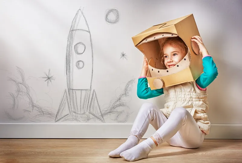kleines Mädchen im Astronautenkostüm sitzt auf dem Boden im Zimmer