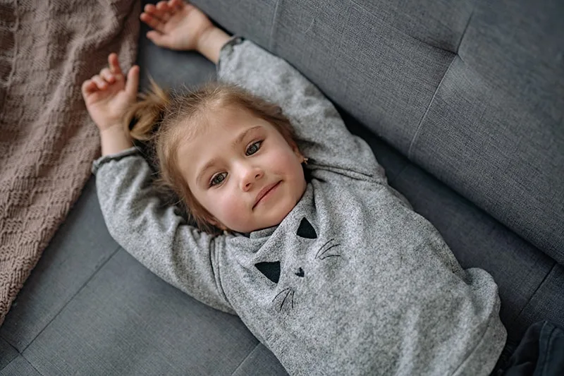 kleines Mädchen im grauen Pullover auf der Couch liegend