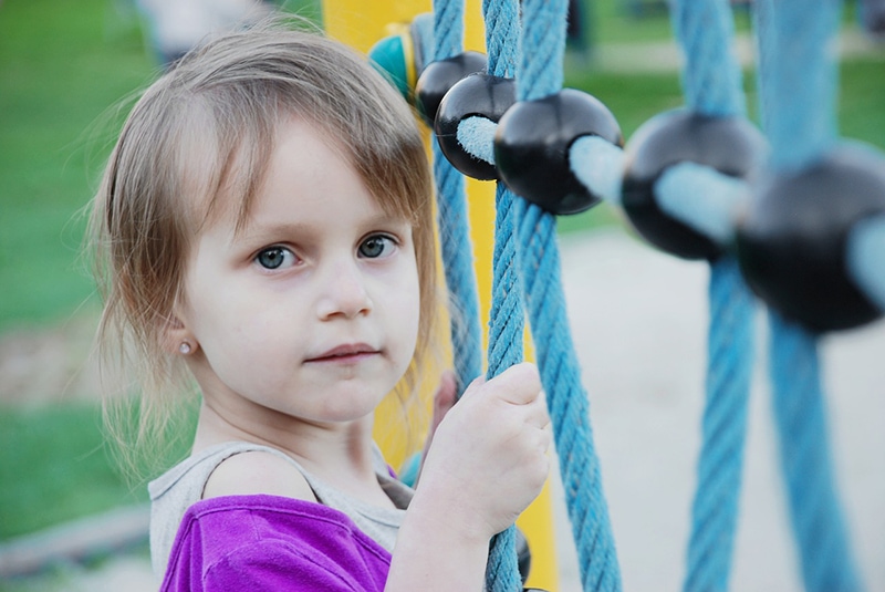 kleines Mädchen in lila T-Shirt Klettern auf Spielplatz