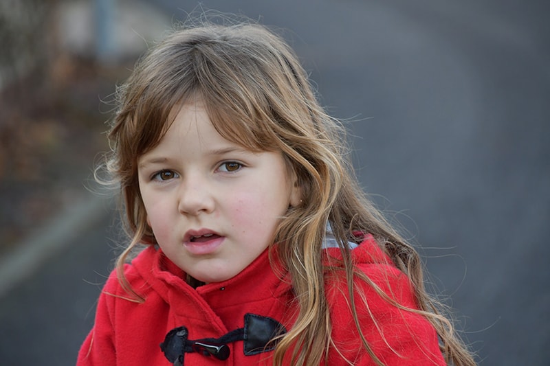 kleines Mädchen im roten Mantel, das auf der Straße steht