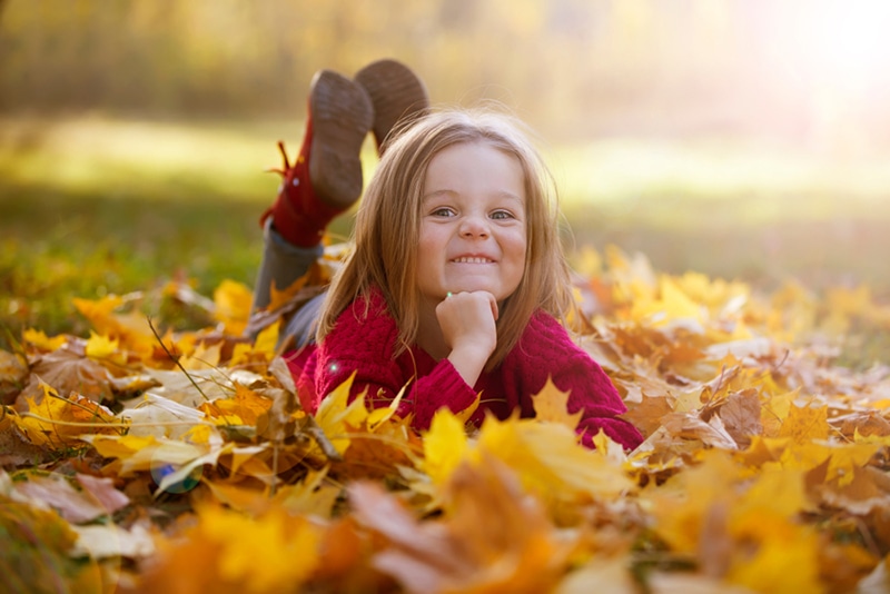 kleines Mädchen liegt auf gelben Blättern im Wald