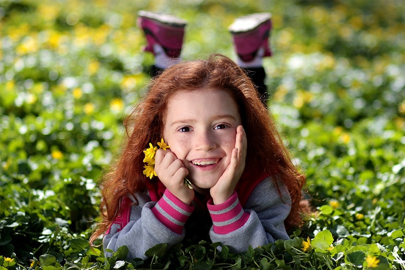 kleines Mädchen liegt im Gras und hält Blumen