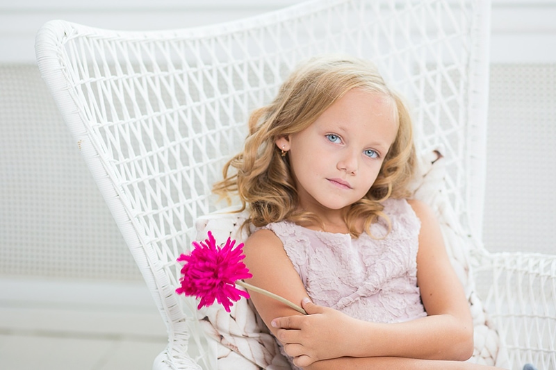kleines Mädchen liegt in einem Sessel und hält rosa Blume