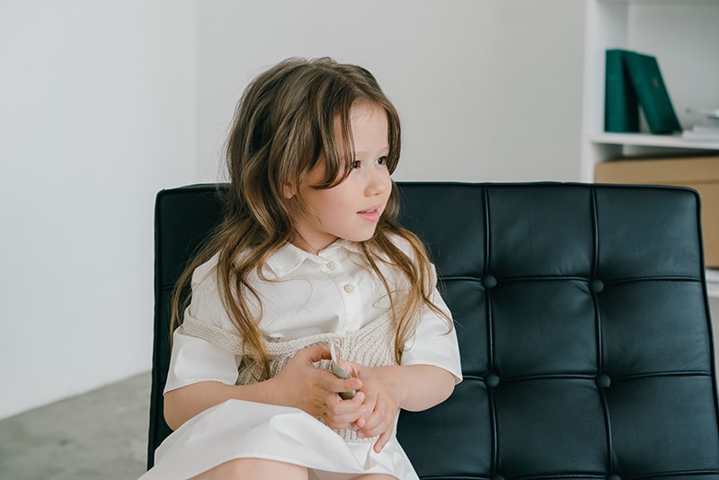 kleines Mädchen mit langen Haaren sitzt auf dem Sofa