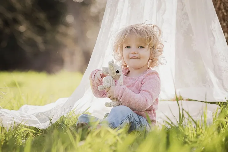 kleines Mädchen sitzt auf dem Gras neben dem Zelt