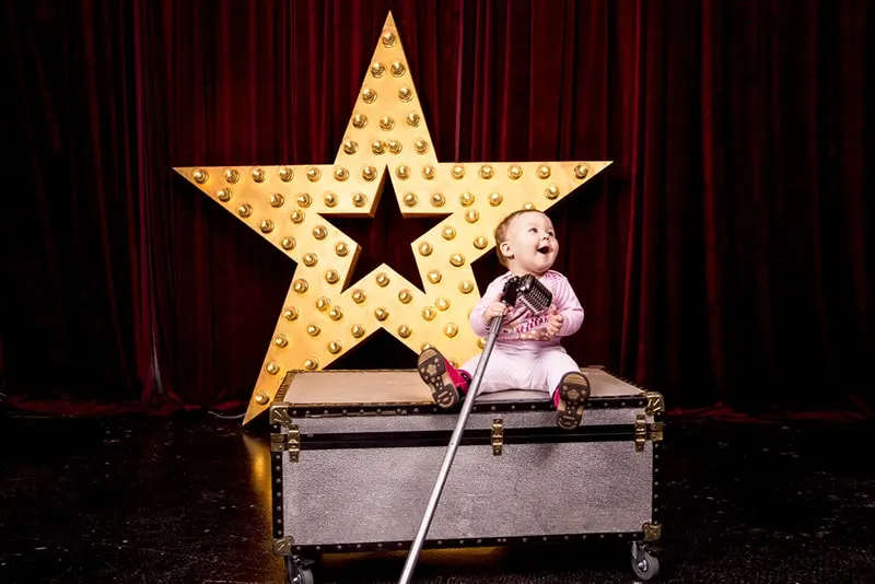 kleines Mädchen sitzt auf der Kiste und singt in ein Mikrofon auf der Bühne
